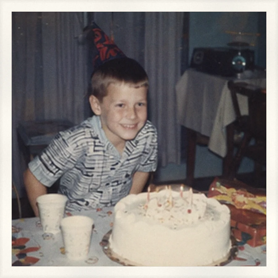 A boy in a party hat behind a birthday cake.