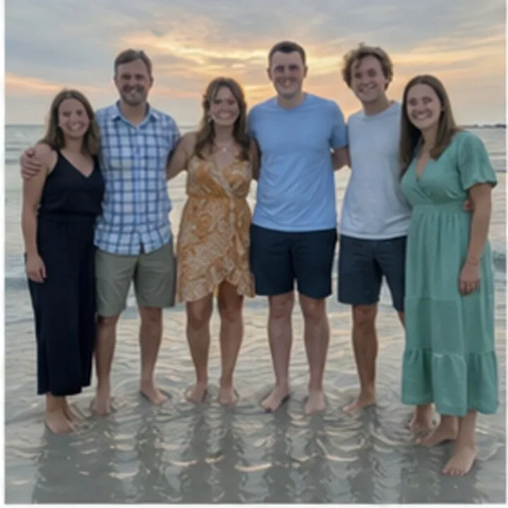 Six young adults standing barefoot in shallow water on a beach at sunset