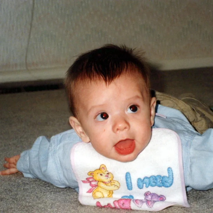 A baby in a bib on the carpet