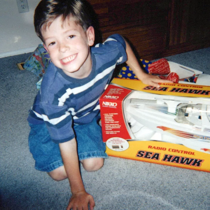 A boy kneeling by a toy boat on his birthday