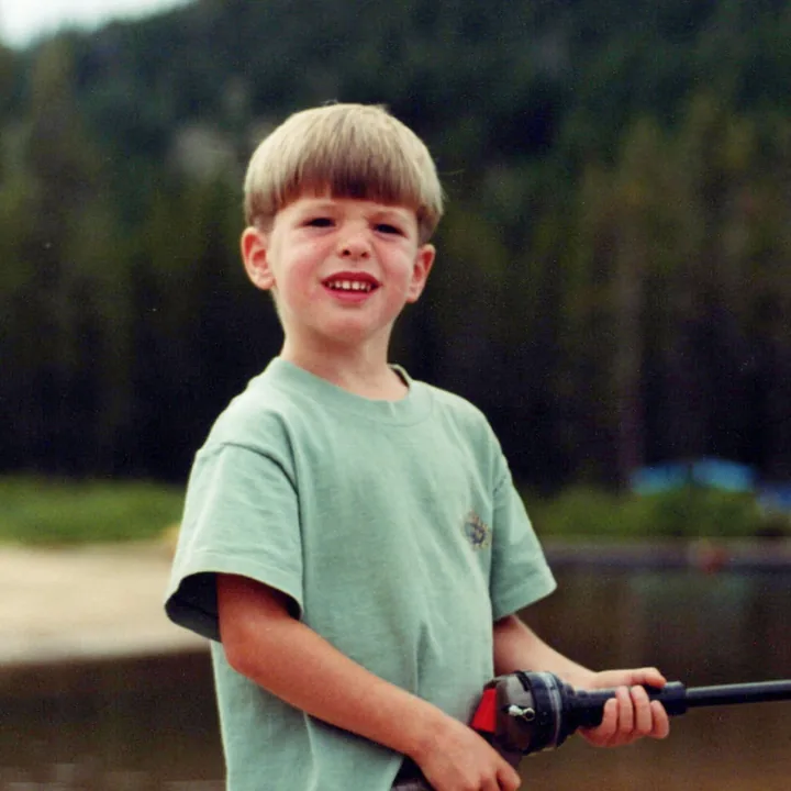A boy holding a fishing rod by a lake
