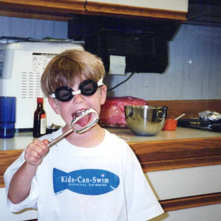 A boy in swim goggles licking a mixer beater